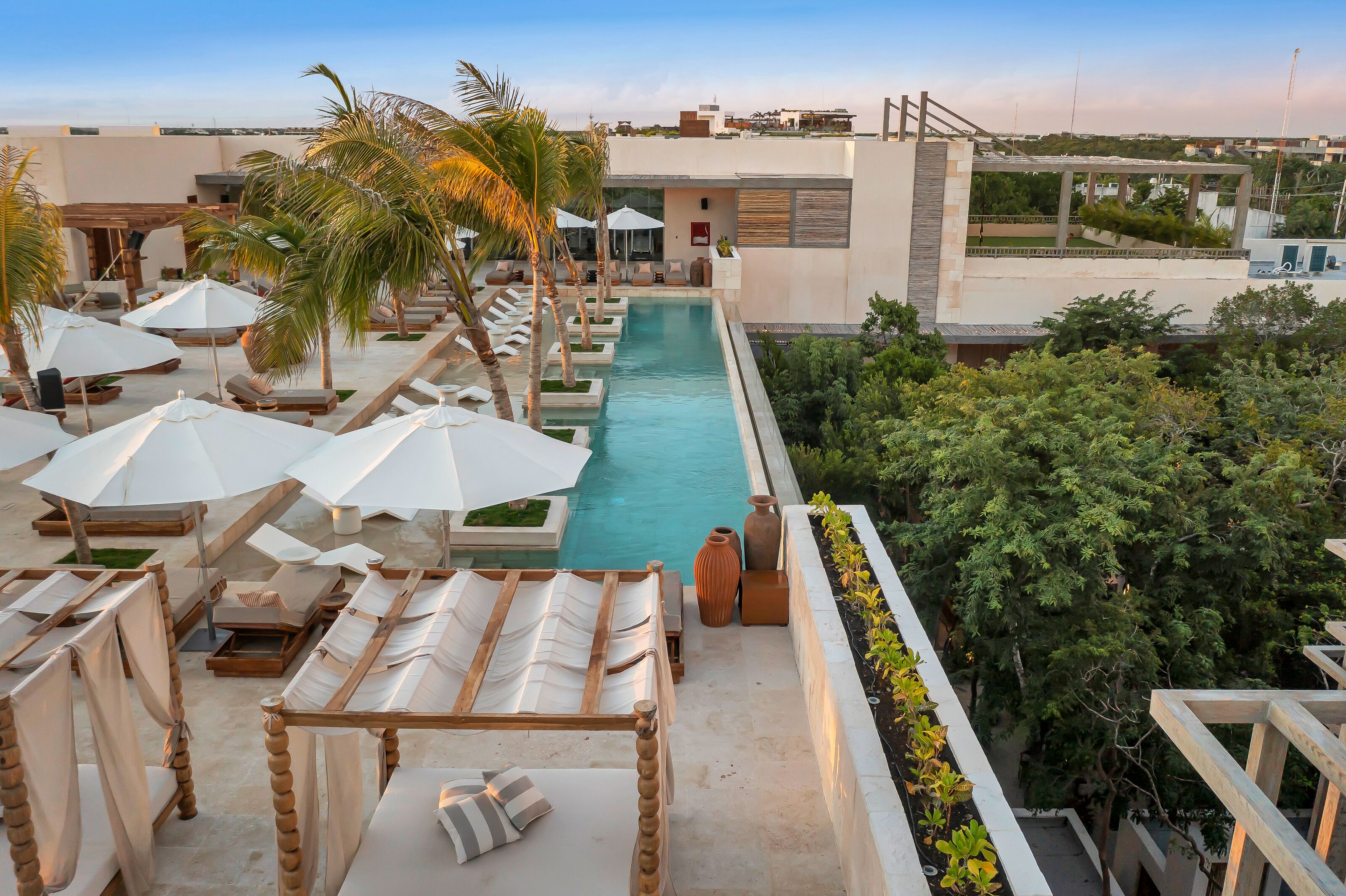 A rooftop pool area with lounge chairs and umbrellas, surrounded by greenery and modern architecture.