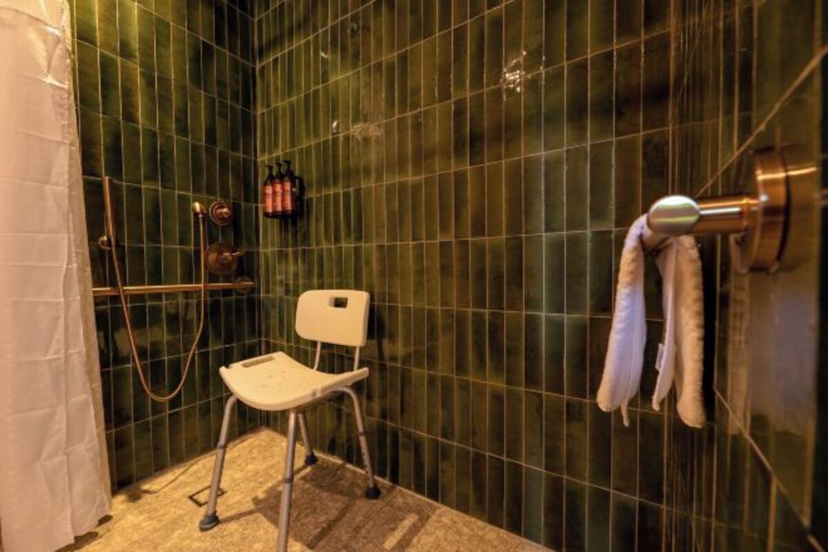 Un área de ducha con una silla blanca, un perchero y un cabezal de ducha.