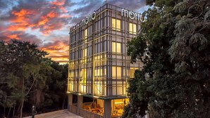 A modern building with a grid-like facade and illuminated windows, surrounded by trees. - Motto by Hilton Tulum (Tulum)
