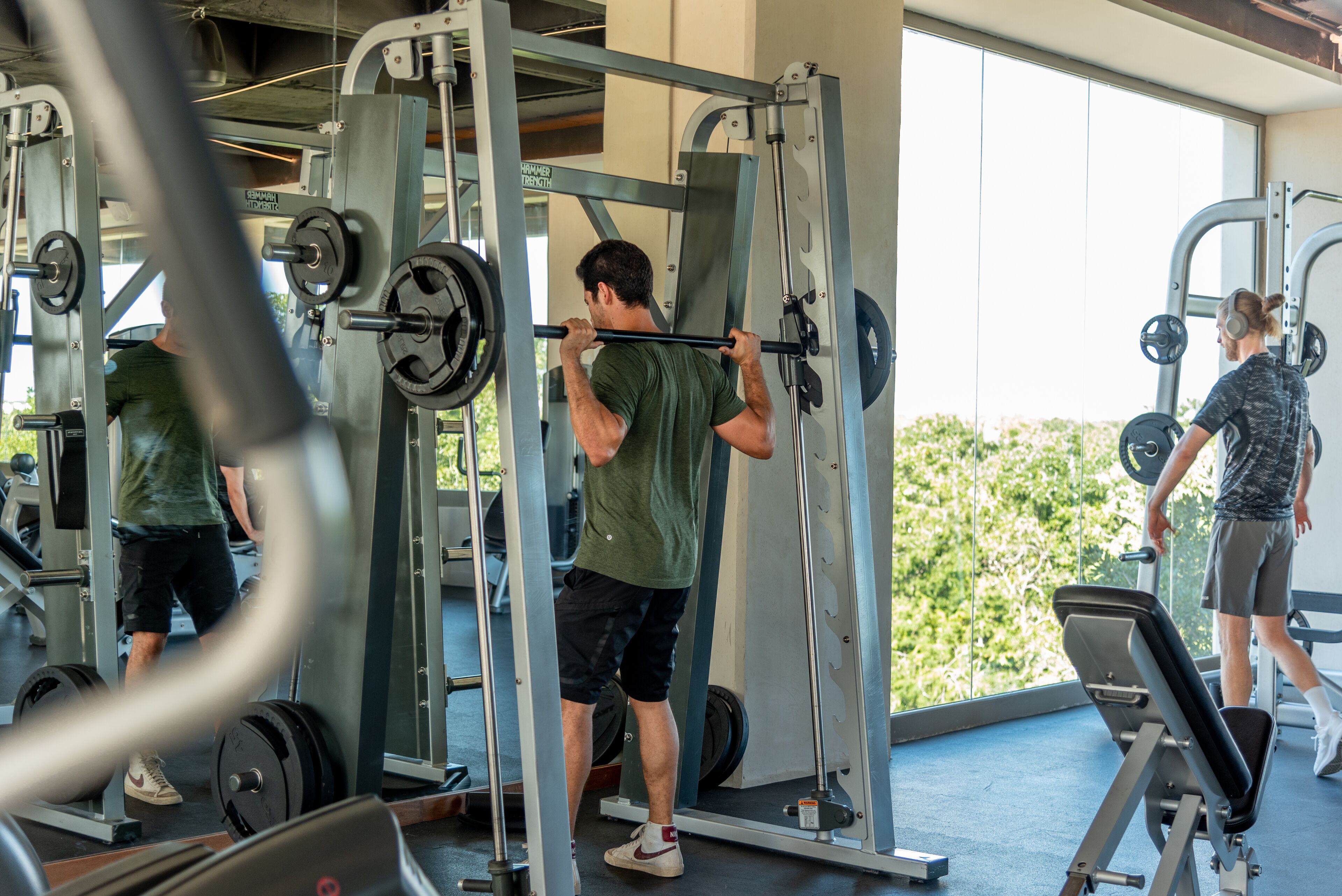 Un gimnasio con equipo de levantamiento de pesas, una cinta de correr y un amplio ventanal con vistas a zonas verdes.