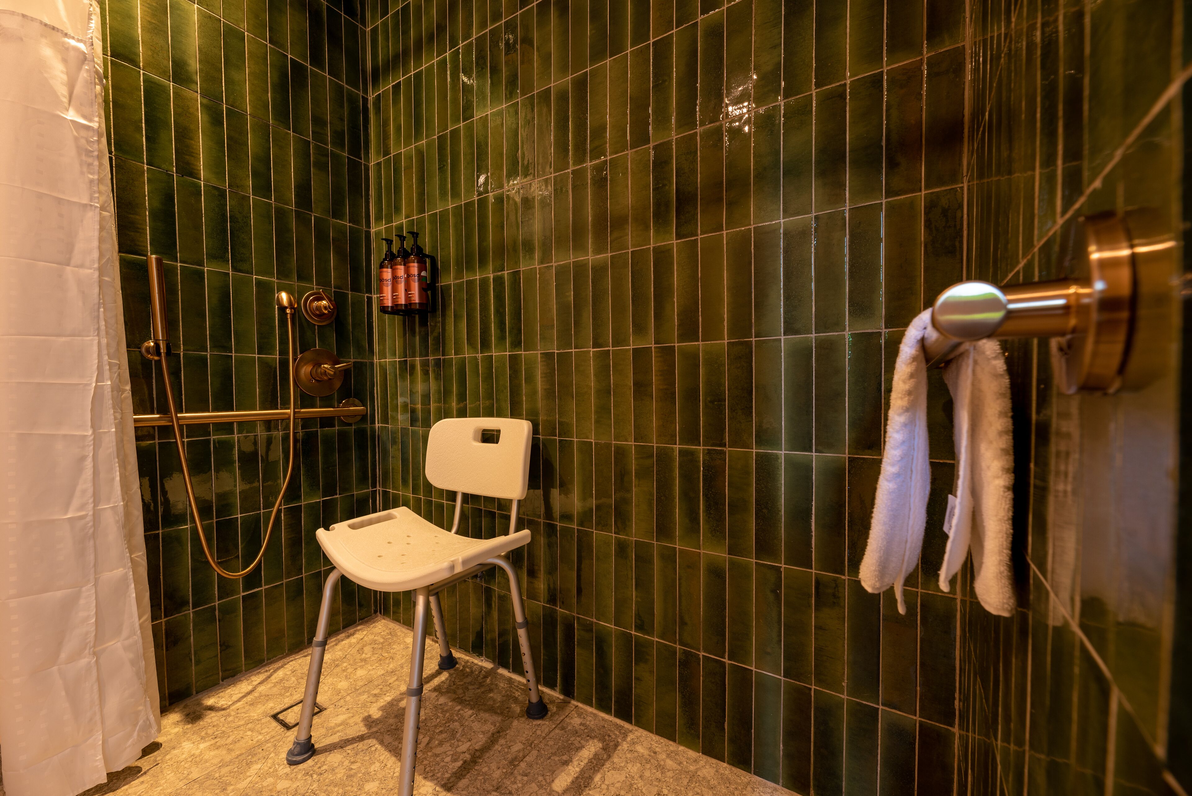 A bathroom with a shower, a white chair, and a towel rack.