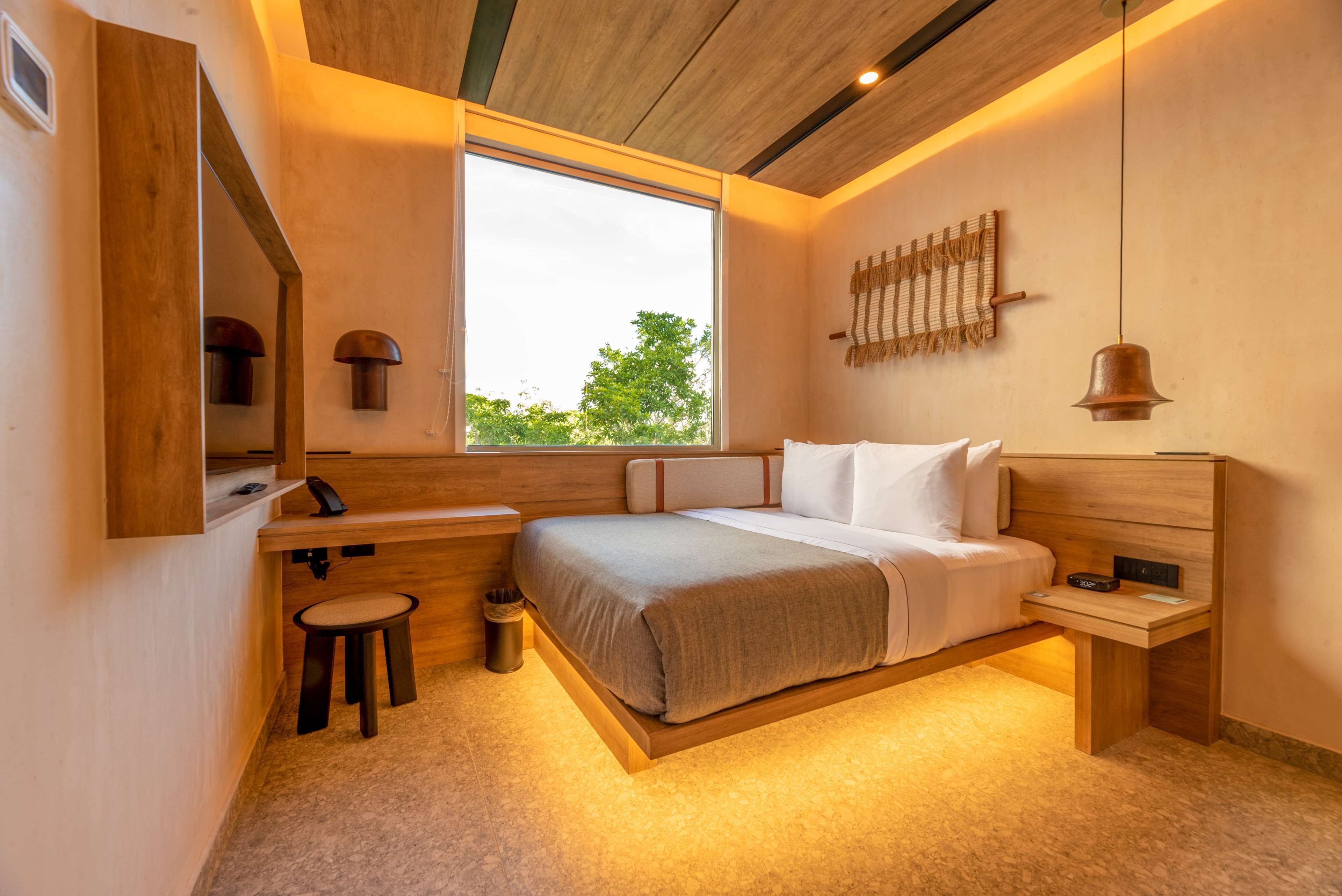 A modern bedroom with a large window, wooden headboard, bedside tables, and a small stool.