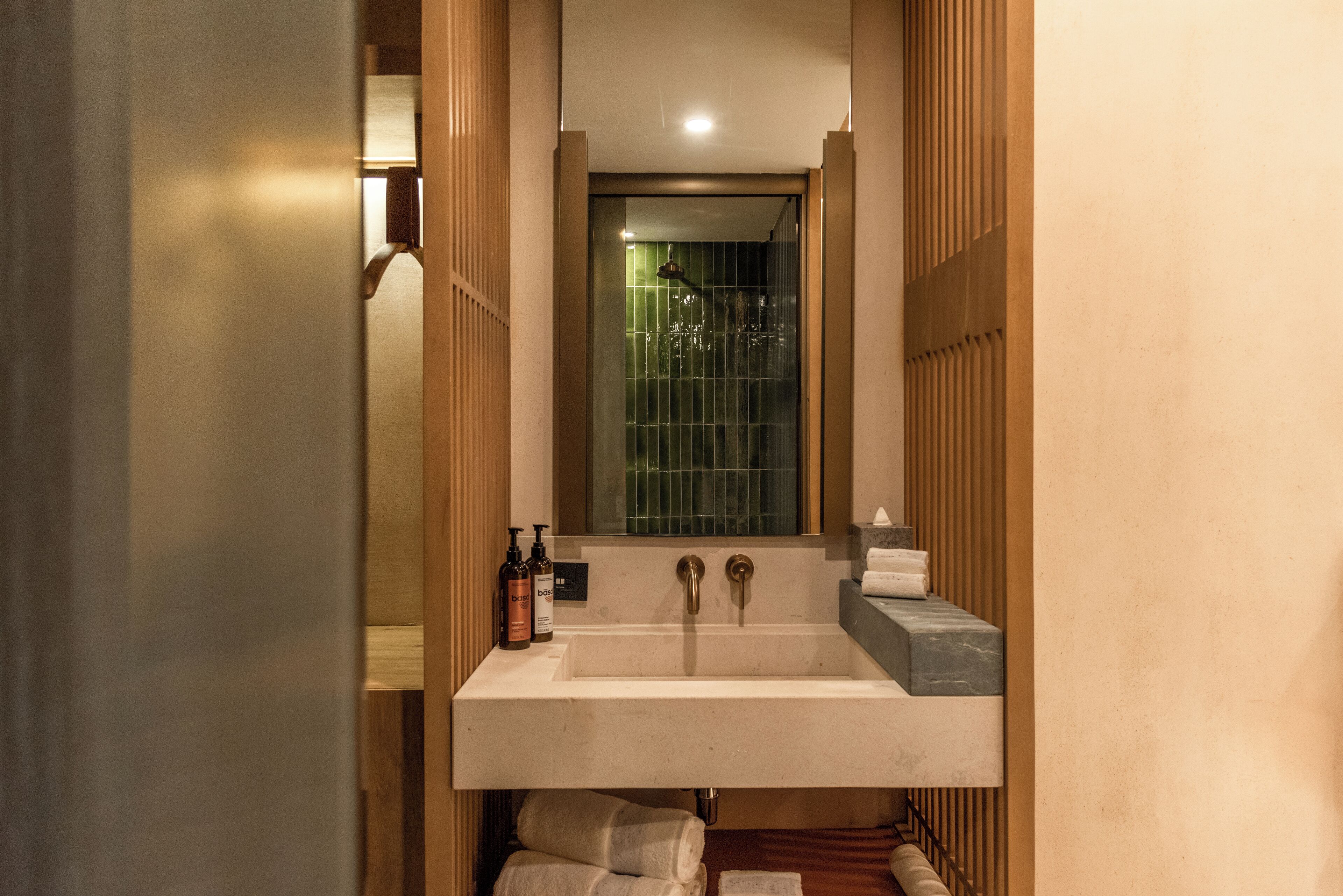 Une salle de bain avec un grand lavabo, deux robinets et un miroir au-dessus. On y trouve des bouteilles sur le lavabo et des serviettes accrochées au mur.