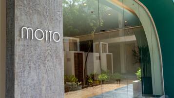 Una entrada de edificio moderno con fachada de vidrio y el nombre 'MOTTO' exhibido en un pilar.