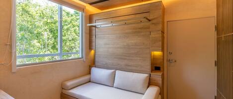 Una habitación moderna con techo de madera, sofá empotrado con cojines, una mesa redonda y ventana con vista a árboles.