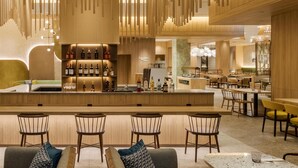 Zona de bar moderna con barra central, diferentes disposiciones de asientos y exhibición de vinos.
