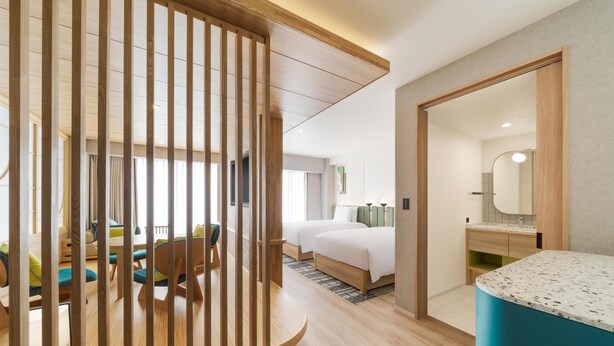 Habitación de hotel con separador de madera, una cama, baño con espejo y zona de comedor con sillas y mesa.