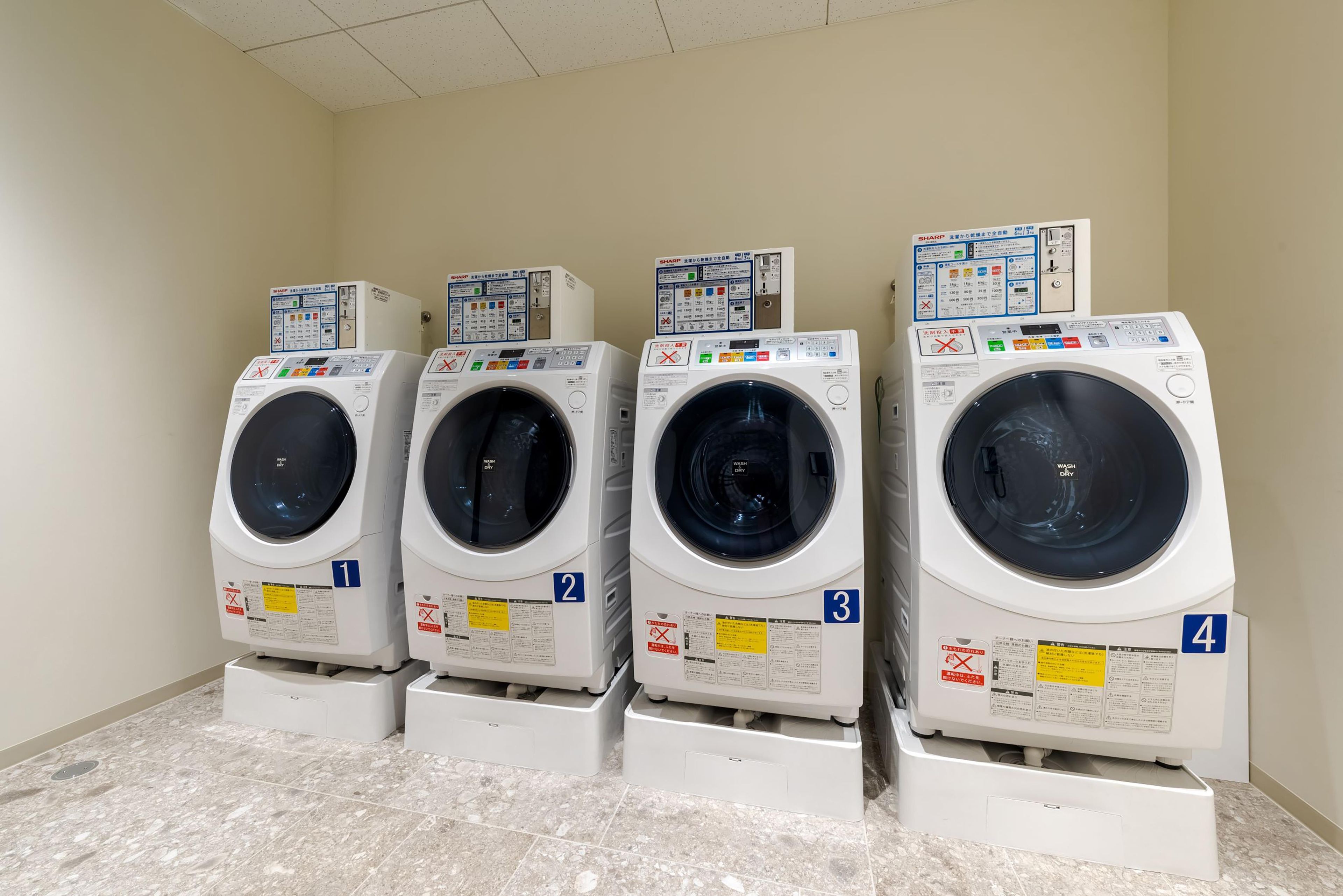 Four stacked front-loading washing machines in a laundry room with numbered labels.