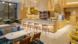 Un área de bar moderna con mostrador de madera, taburetes y un espacio de estar con mesas y sillas.
