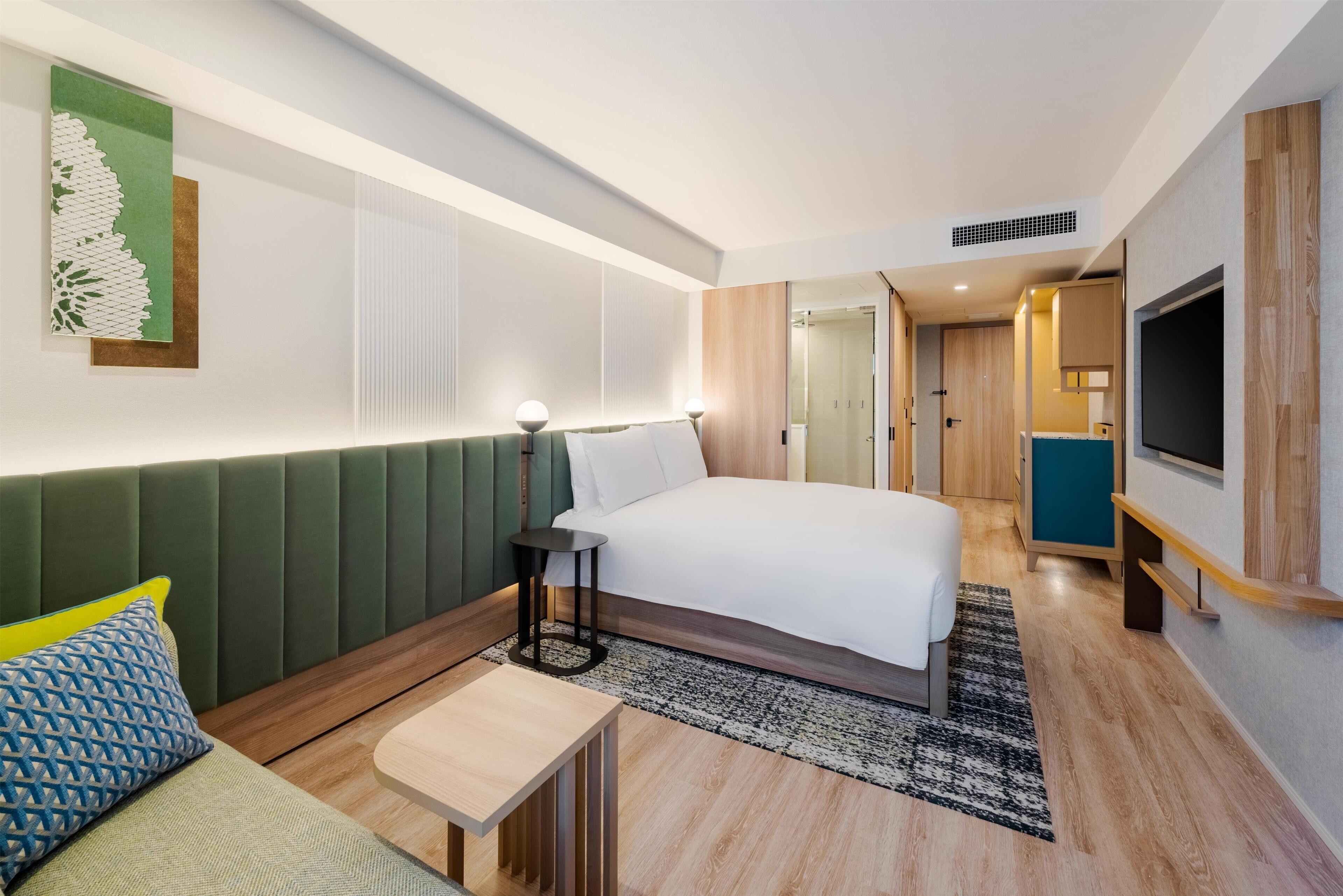 A modern hotel room with a bed, bedside table, lamp, and a television.