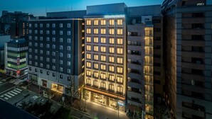 Un hotel de varios pisos con fachada moderna, ventanas iluminadas y entrada visible.