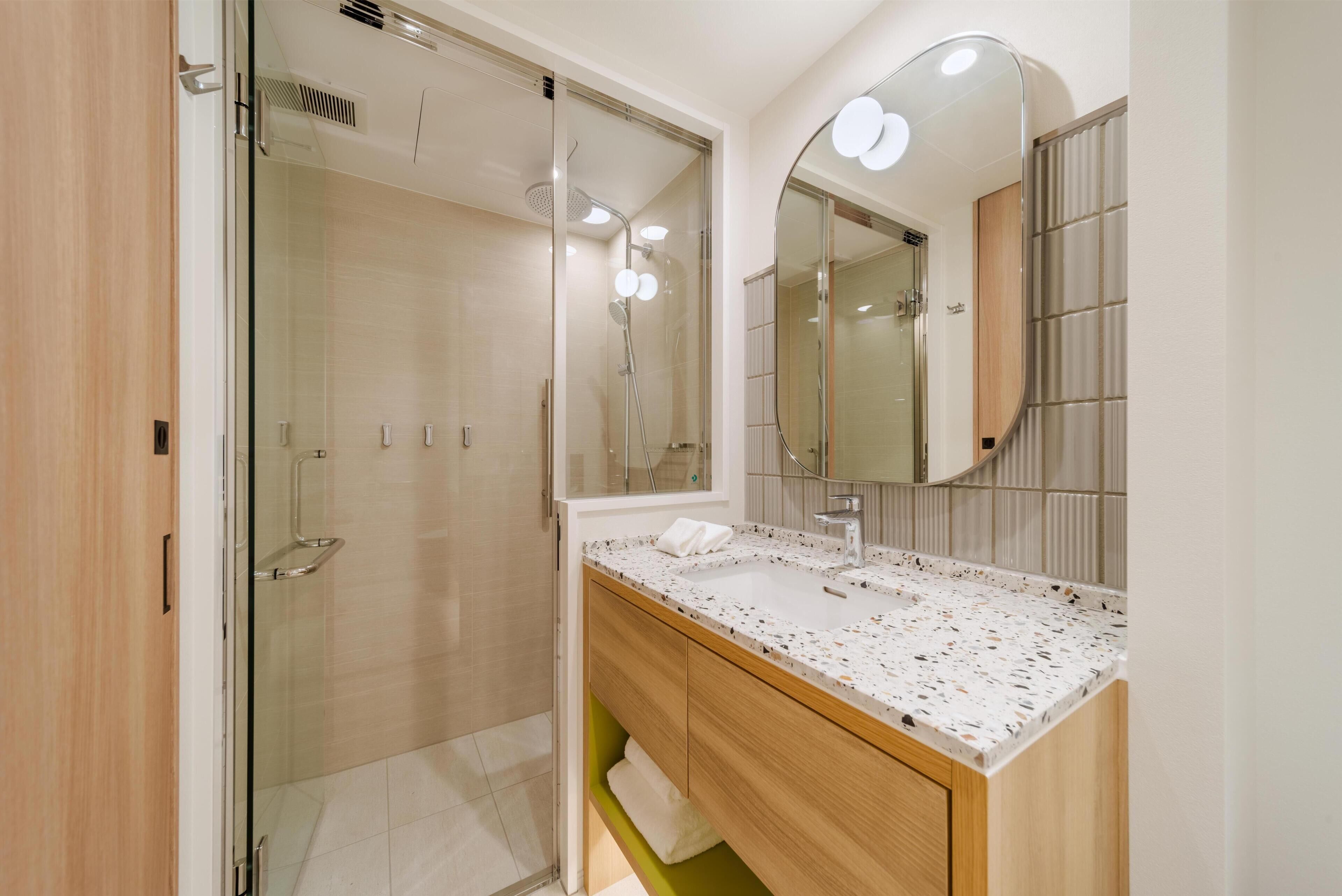 A modern bathroom with a glass shower enclosure, a freestanding sink, and a large mirror with integrated lighting.
