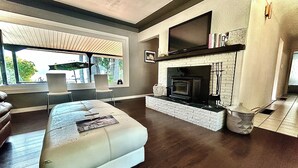 A modern living room with a fireplace, a sofa, and a television mounted above it. - West House! A beautiful lake front home with hot tub and dock. (Shawnigan Lake)
