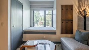 Une pièce de taille modeste, dotée d’un coin fenêtre aménagé en siège, d’une petite table, d’un canapé et d’une armoire en bois.