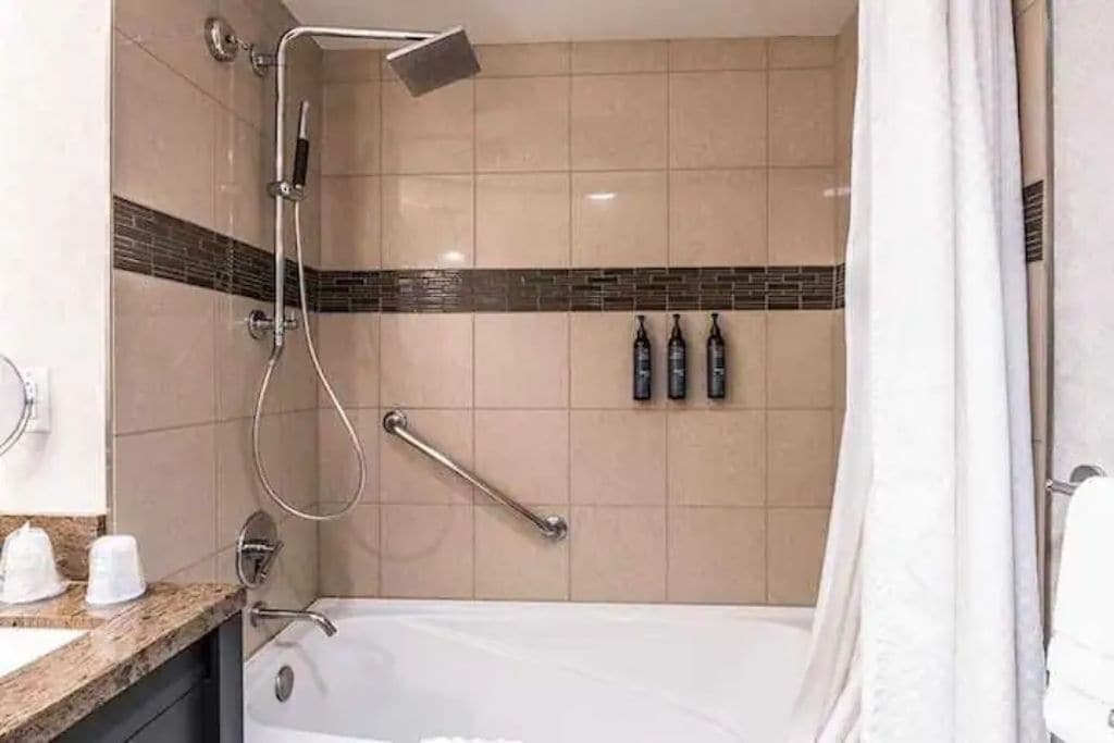 Ein Badezimmer mit Badewanne, Dusche und Handlauf. An der Wand befinden sich drei Flaschen.