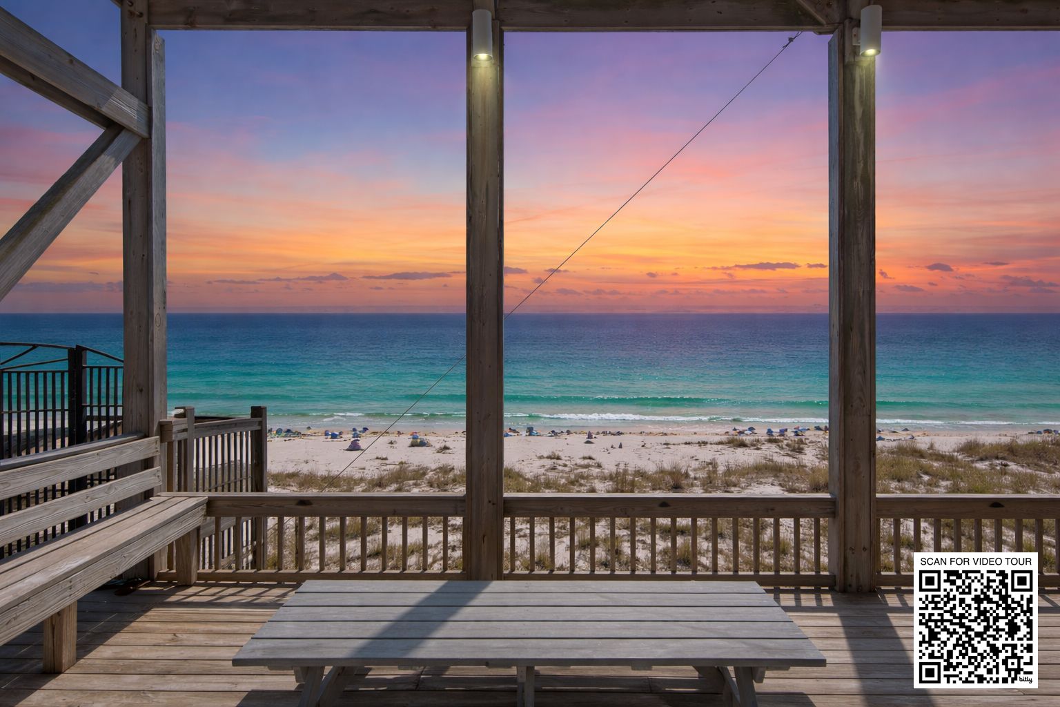 A wooden deck with a view of a beach and ocean during sunset.