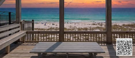 A wooden deck with a view of the beach and ocean at sunset.