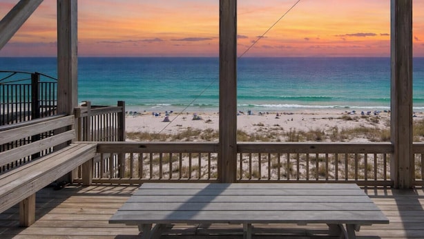 Eine Holzterrasse mit Blick auf einen Strand und das Meer bei Sonnenuntergang.
