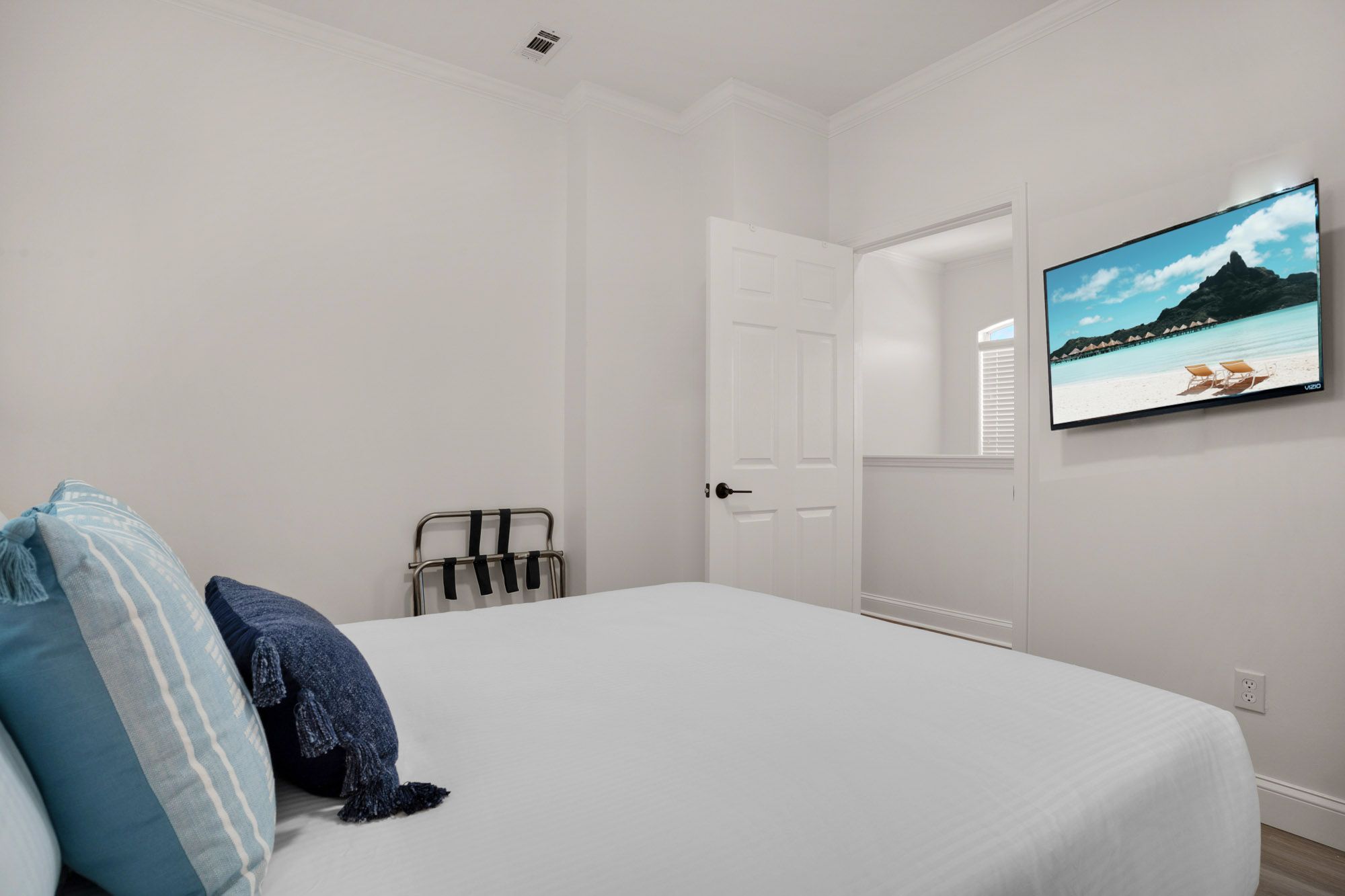 A bedroom with a bed, a TV on the wall, and a door leading to another room.