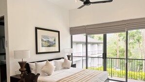 A hotel room with a large bed, a desk, a chair, a ceiling fan, and a balcony with a view of greenery. - The Lavender House by Reveal (Pussellawa)