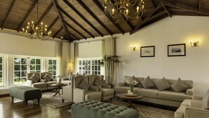 A spacious living room with a high ceiling, wooden beams, and a chandelier. There are multiple sofas and a large ottoman. - The Lavender House by Reveal (Pussellawa)
