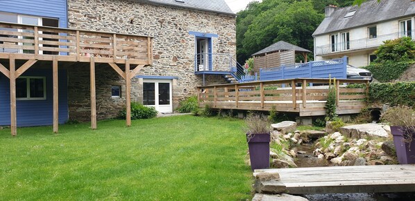 A stone building with a wooden deck, a small pond, and a stone wall.