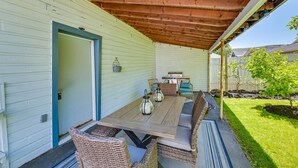 Een terras buiten met een houten tafel, rieten stoelen, een deur en een kleine tuin.