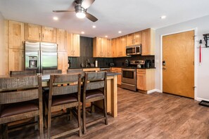 A modern kitchen with wooden cabinets, stainless steel appliances, and a dining area with wooden chairs.
