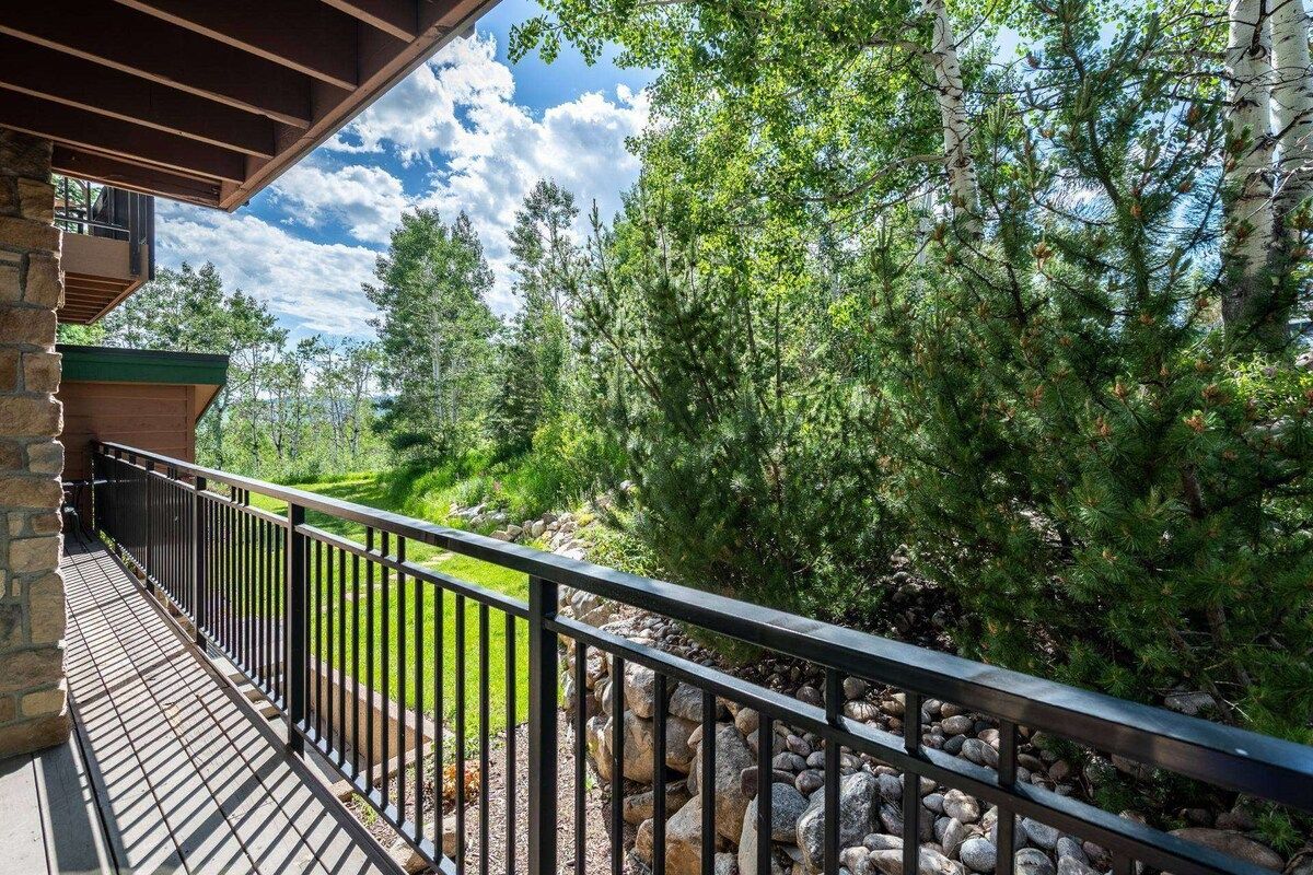 A balcony with a stone wall, metal railing, and a view of a forested area.