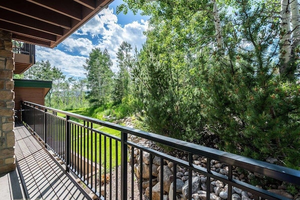 A balcony with a stone wall, metal railing, and a view of a forested area.