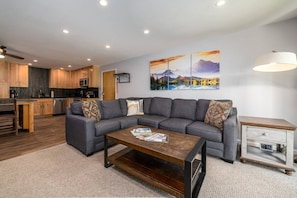 A modern living room with a gray sectional sofa, a wooden coffee table, and a small side table.