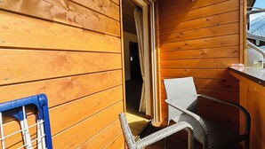 Interno di una baita in legno con una sedia in vimini, un tavolino e una finestra che si affaccia su montagne innevate.