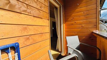 Ein Interieur einer Holzhütte mit einem Korbsessel, einem kleinen Tisch und einem Fenster mit Blick auf schneebedeckte Berge.