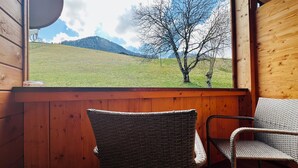 Una baita di legno con sedie in vimini e vista su un prato e montagne.