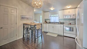 A modern kitchen with white cabinetry, a central island with stools, a chandelier, and built-in appliances. - Breezy Coloma Getaway w/ Grill - 1 Mi to Beaches! (Coloma)