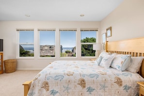 A bedroom with a large bed, multiple windows, a television, and a lamp. - Spacious Ocean-View Home with Fireplace, Foosball, and Fire-pit, Huge Patio, Steps to the Beach (Cloverdale)