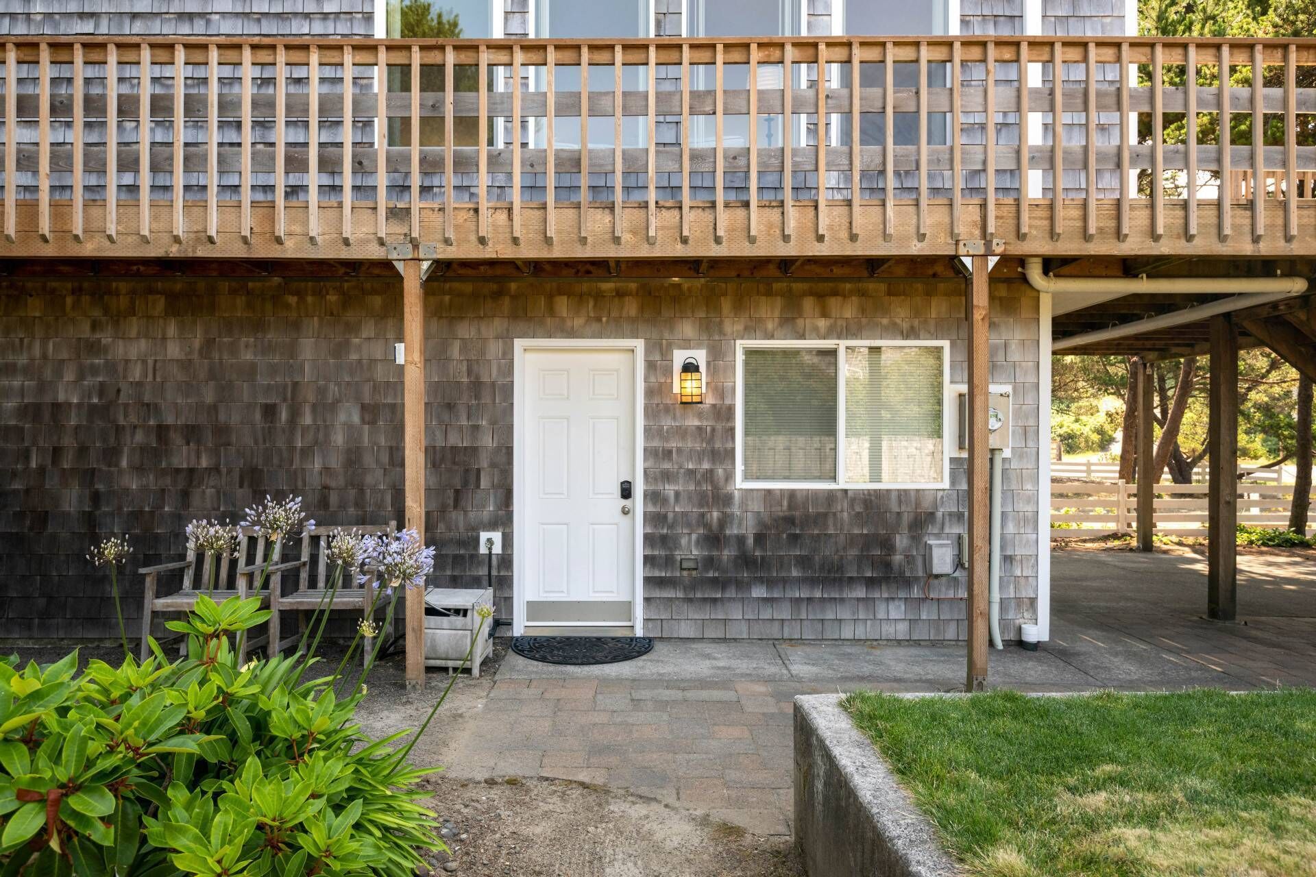 Un bâtiment à deux étages doté d’un balcon en bois, d’une porte d’entrée et d’un petit porche avec un banc et des plantes en pot.