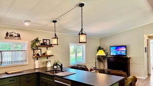 A spacious kitchen with a central island, pendant lights, and a television in the living area. - Riverfront Gem with Big Deck, Fishing & Adventure. Comfy beds, upgraded beauty (Trail)