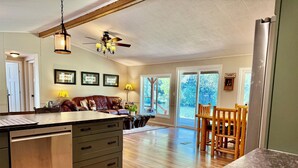 A spacious kitchen with a large island, wooden flooring, and a ceiling fan. - Riverfront Gem with Big Deck, Fishing & Adventure. Comfy beds, upgraded beauty (Trail)