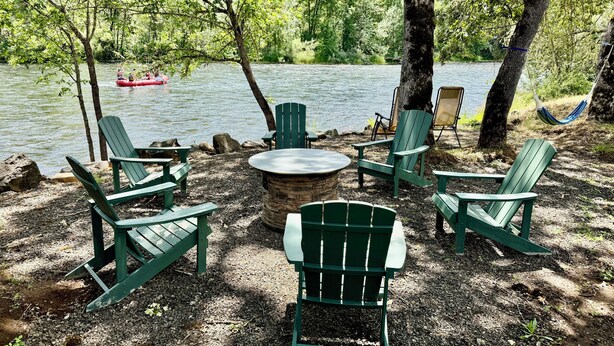A lakeside seating area with Adirondack chairs and a fire pit. - Riverfront Gem with Big Deck, Fishing & Adventure. Comfy beds, upgraded beauty (Trail)