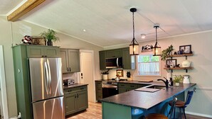 A modern kitchen with a central island, stainless steel appliances, and a bar area with stools. - Riverfront Gem with Big Deck, Fishing & Adventure. Comfy beds, upgraded beauty (Trail)