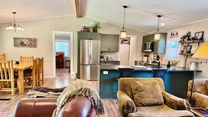A spacious living room with leather sofas, a dining area, and a kitchen with modern appliances. - Riverfront Gem with Big Deck, Fishing & Adventure. Comfy beds, upgraded beauty (Trail)