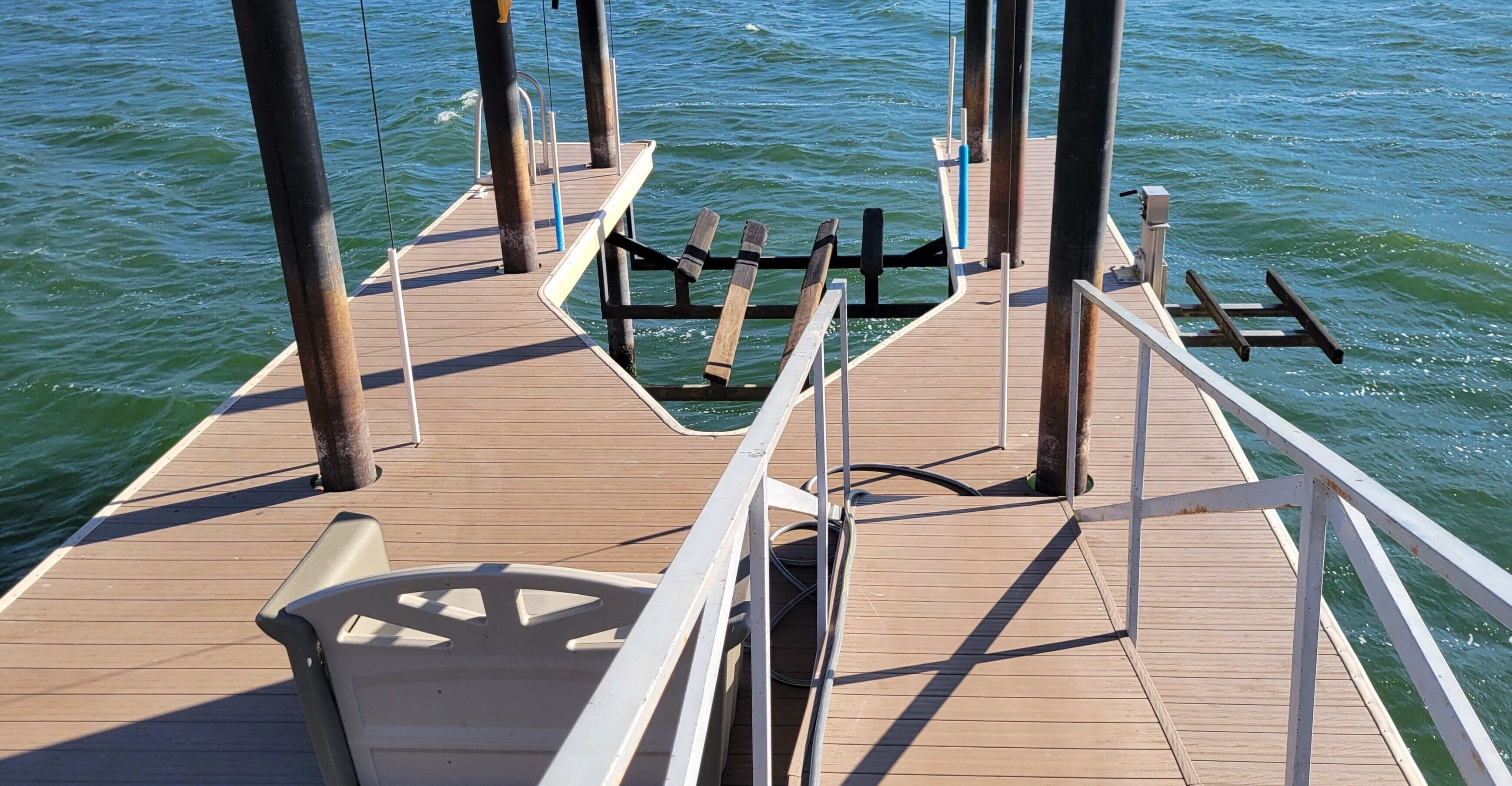 A wooden pier extending into a body of water with a metal railing and a single chair.