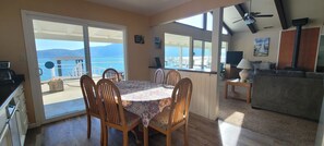 A dining area with a table and chairs, a kitchen area with a TV, and a view of the sea through large windows.