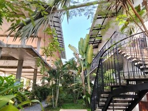 Espaço ao ar livre com vários níveis, incluindo uma escadaria, cercado por vegetação exuberante e edifícios com varandas.