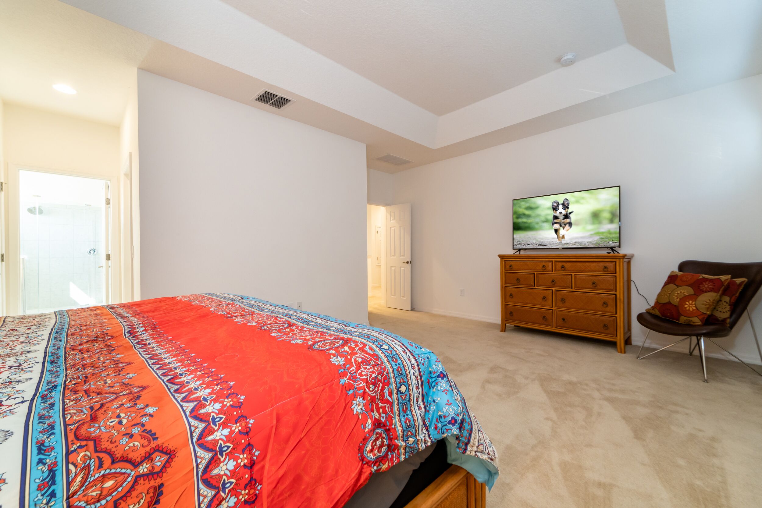 Een slaapkamer met een groot bed, een houten dressoir, een televisie aan de muur en een deur naar een andere kamer.