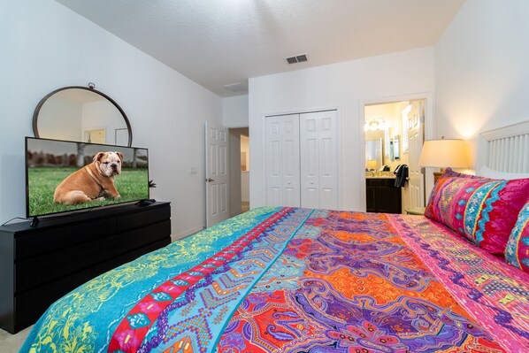 A bedroom with a large bed, a TV on a dresser, and a door leading to a bathroom. - Pool Home With Spa In Golfing Community With Resort Amenities (Davenport)