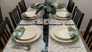 A dining table set for six with white plates, green glassware, and a bottle of Charles Wine.