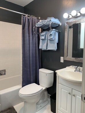 Un baño con inodoro blanco, bañera, lavamanos con espejo y cortina de ducha.