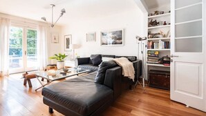 A modern living room with a black leather sofa, a glass coffee table, and a bookshelf.